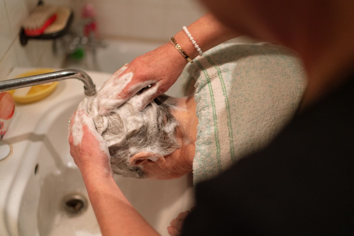 A caregiver gently assisting a senior client with personal care at home